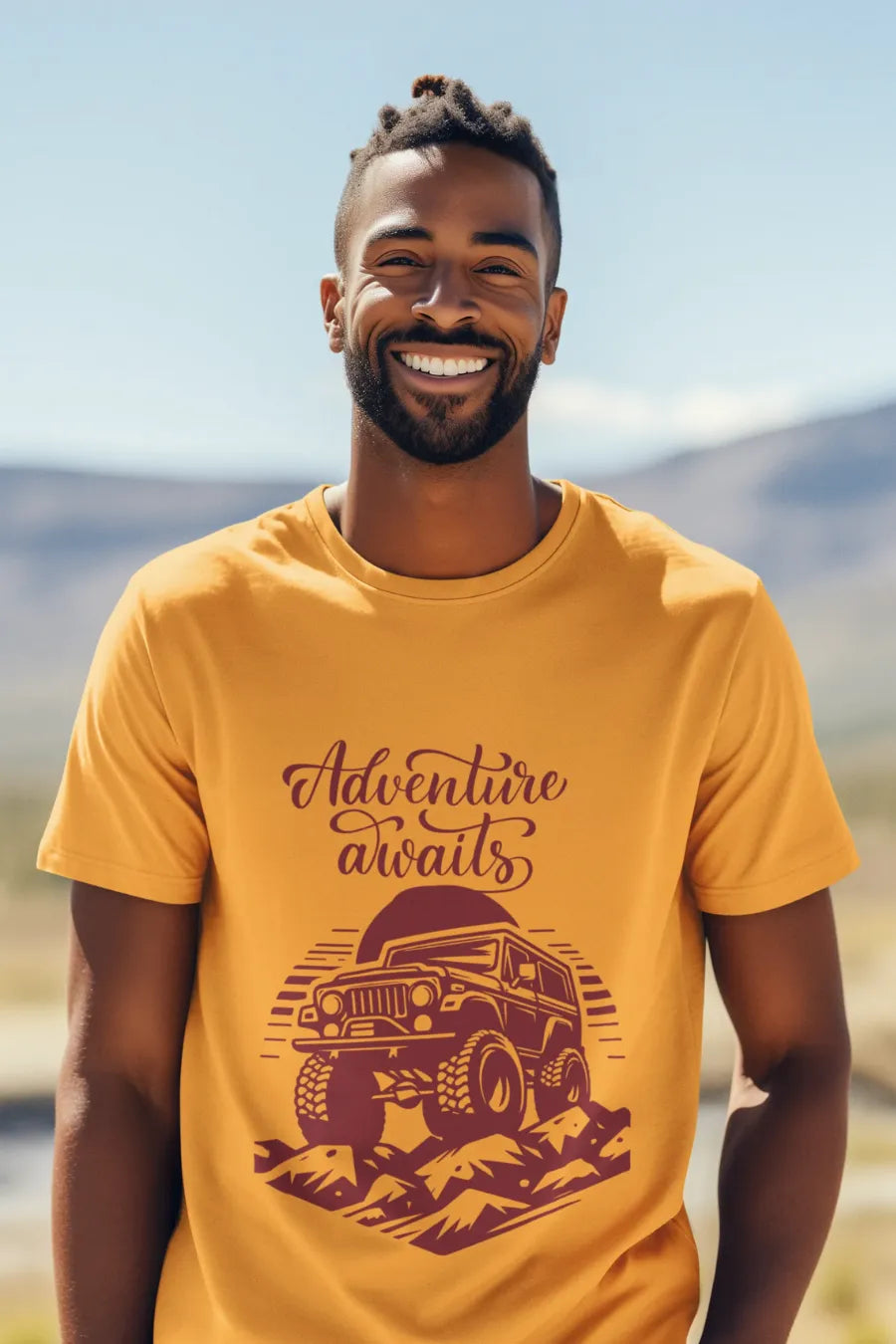 Man wearing a mustard yellow T-shirt with a rugged jeep and 'Adventure Awaits' text graphic, standing outdoors with a mountain background.