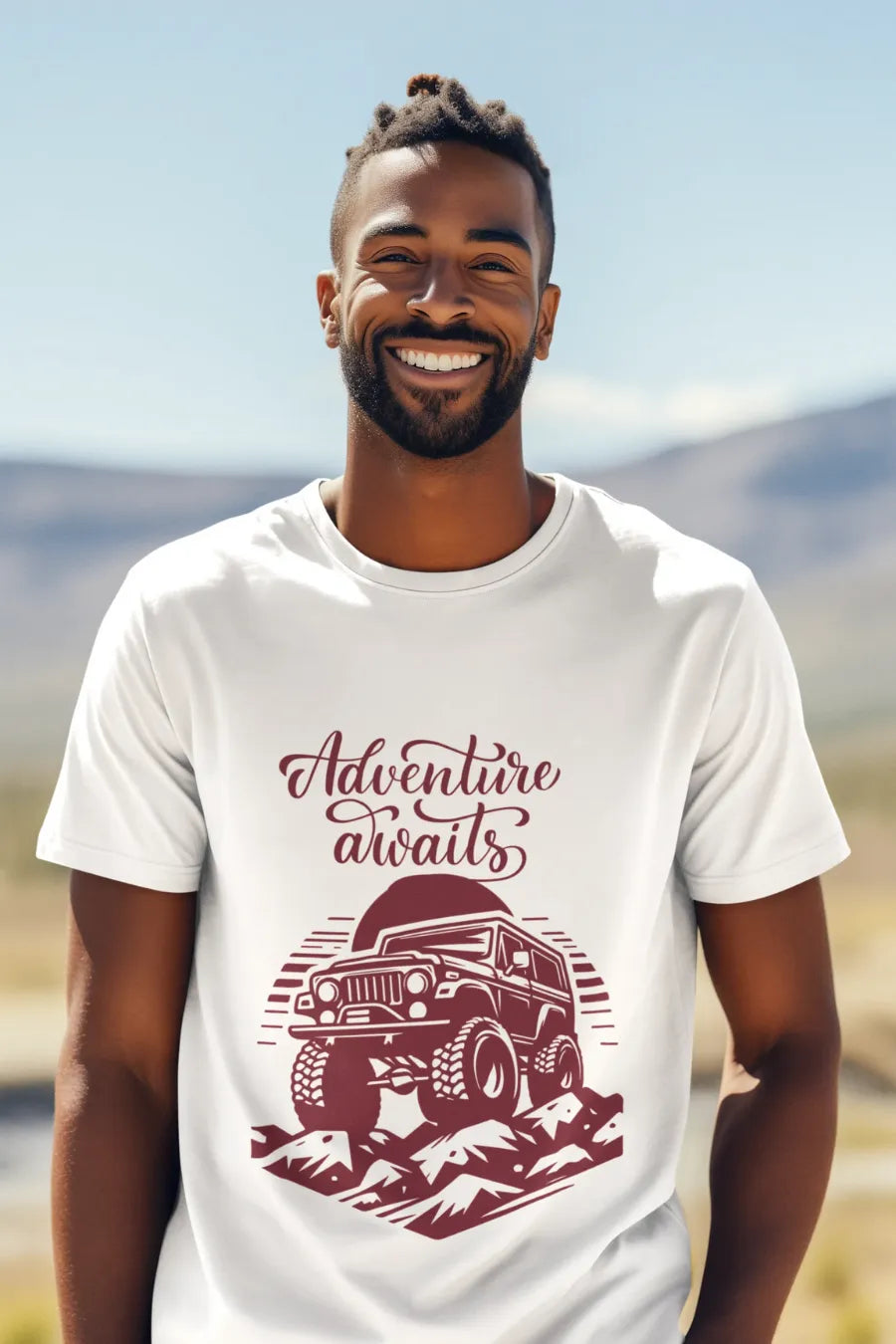 Man wearing a white T-shirt with a rugged jeep and 'Adventure Awaits' text graphic, standing outdoors with a mountain background.