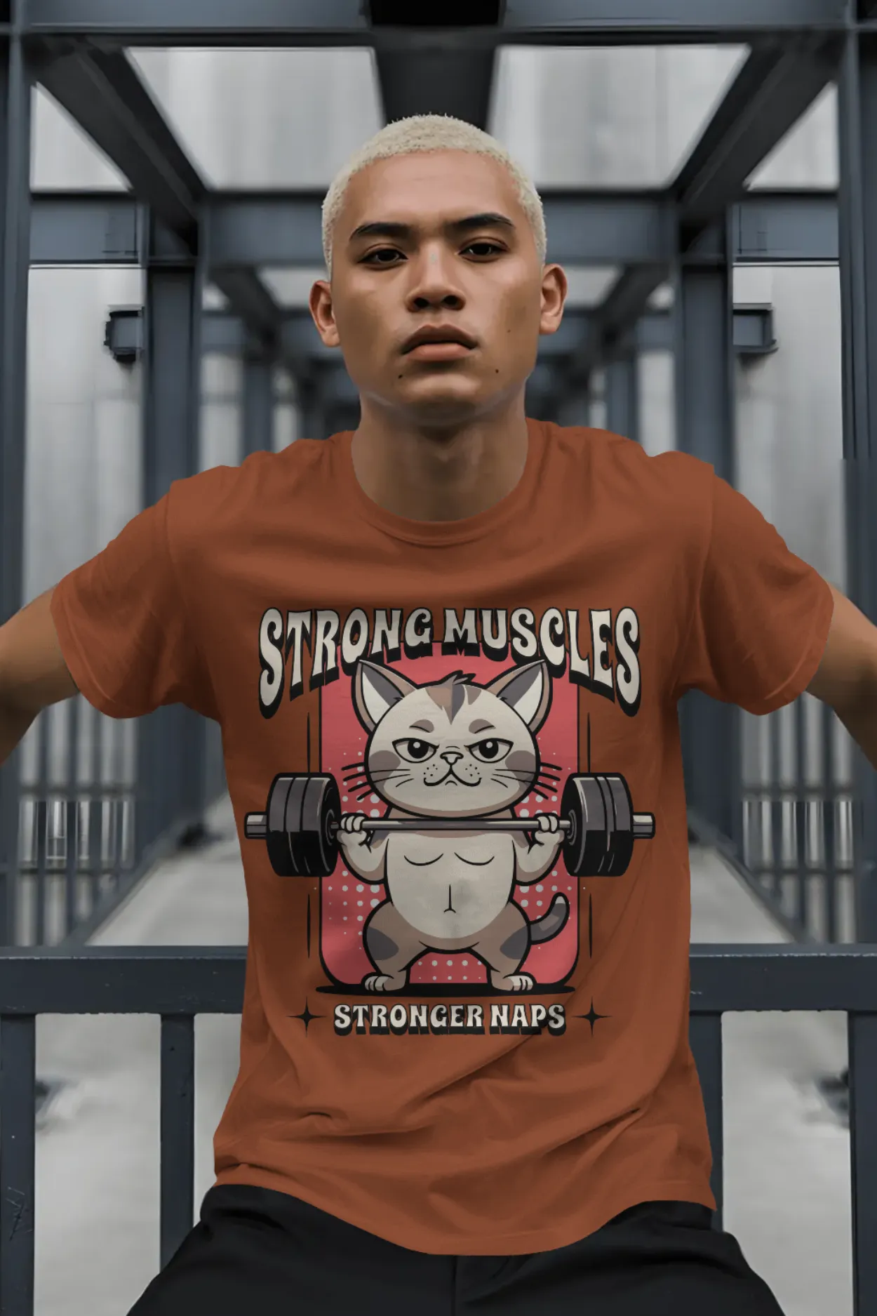 Man wearing rust brown graphic tee with a muscular cat lifting weights and the quote “Strong Muscles Stronger Naps” printed on the front.