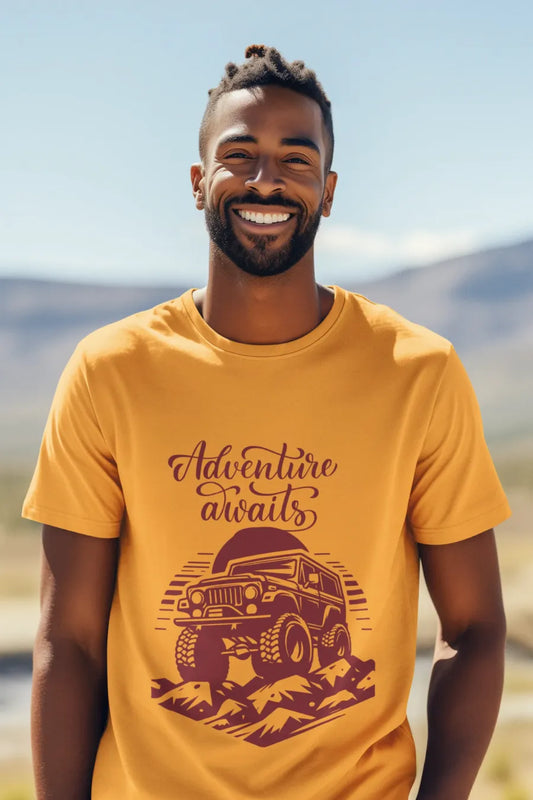 Man wearing a mustard yellow T-shirt with a rugged jeep and 'Adventure Awaits' text graphic, standing outdoors with a mountain background.