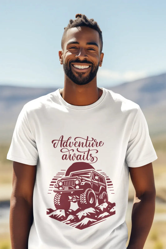 Man wearing a white T-shirt with a rugged jeep and 'Adventure Awaits' text graphic, standing outdoors with a mountain background.