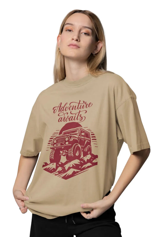 Woman in beige oversized t-shirt with off-road vehicle and 'Adventure Awaits' typography design