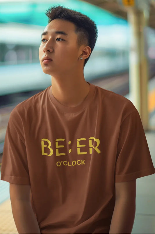 A man wearing a Rust brown cotton t-shirt with yellow 'Beer O’Clock' graphic, worn by male model at a train station.