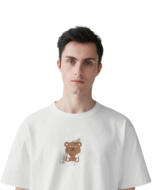 Man wearing an off-white t-shirt featuring Halloween-style graphics like a creepy smiley face, stitched teddy bear, skeleton hands, and words like “Be Brave,” “Cool,” and “Stay Wild” in brown and black ink.