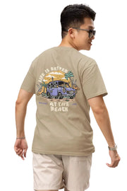 Man wearing a beige brown Double Impact T-shirt with beach skeleton and travel car design.