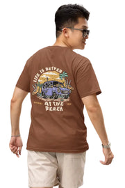 Man wearing a rust brown Double Impact T-shirt with beach skeleton and travel car design