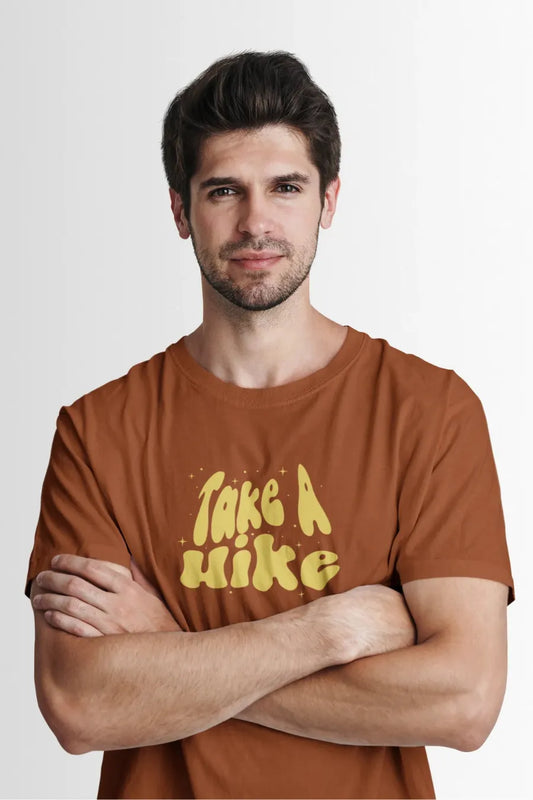 Man wearing a rust brown T-shirt with bold yellow 'Take A Hike' graphic in vintage typography.