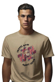 Man wearing a Beige Brown T-shirt with 'Travel Now Adult Later' graphic design featuring sunset, waves, and floral elements